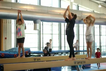 gymnastics 3 girls on a balance beam with their arms stretched upwards